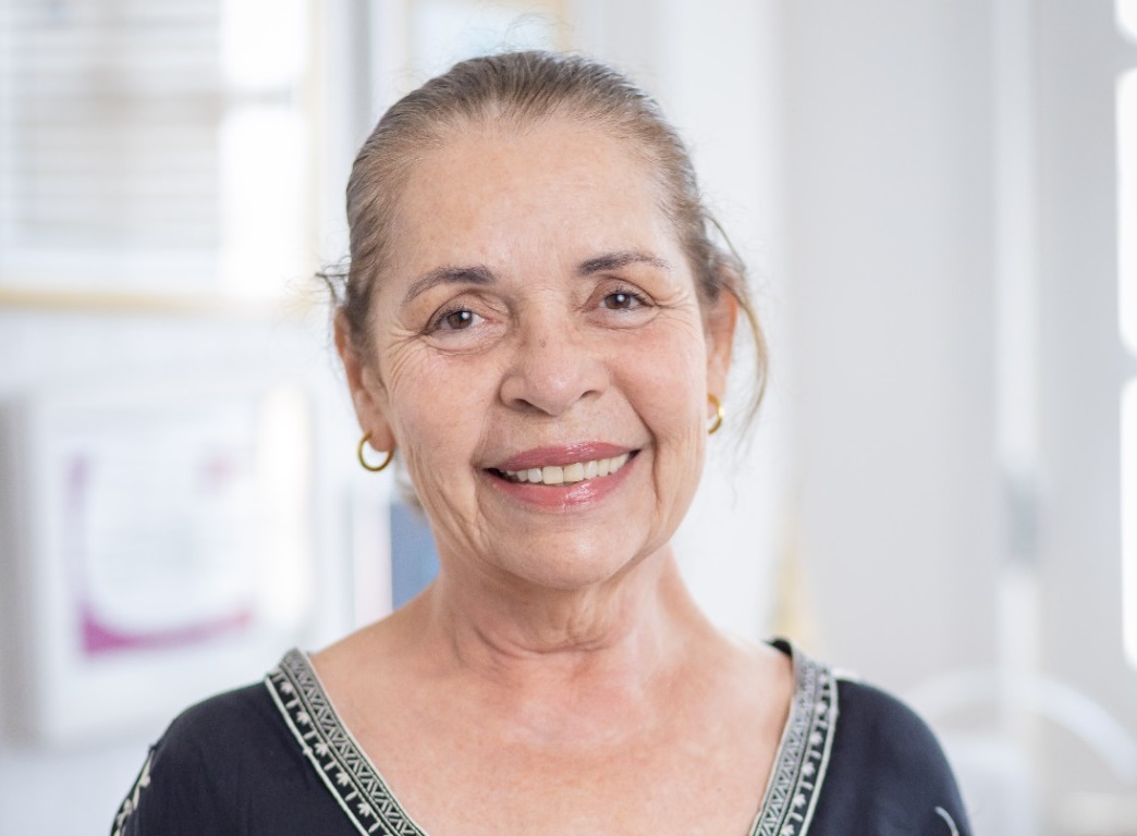 Dora Andrade posa para a foto sorrindo, veste uma blusa preta e está de cabelo preso